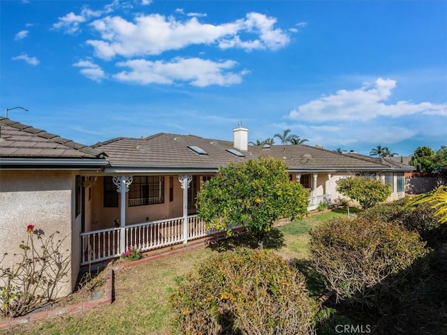 view of front of home featuring a tiled roof, a front lawn, a porch, and stucco siding