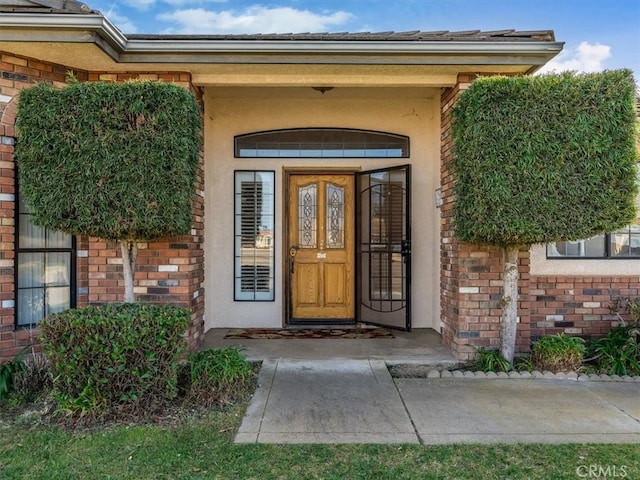 view of exterior entry with brick siding and stucco siding