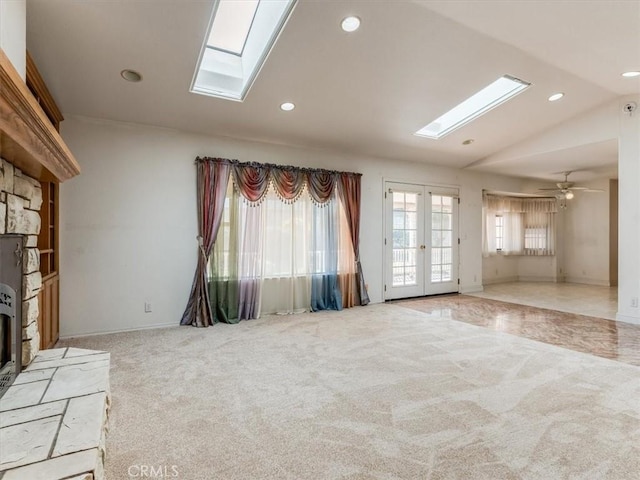 unfurnished living room featuring light carpet, vaulted ceiling with skylight, recessed lighting, and french doors