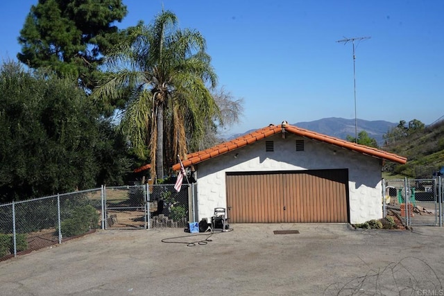 view of outdoor structure featuring a gate, fence, a mountain view, and an outbuilding