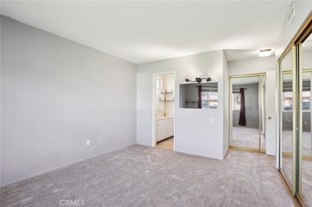 unfurnished bedroom featuring light carpet, connected bathroom, visible vents, and two closets