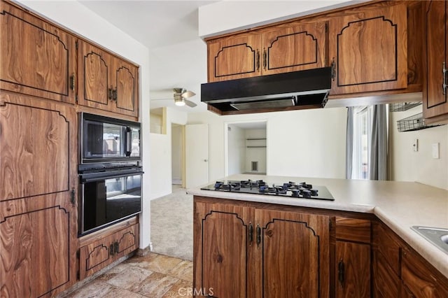 kitchen featuring brown cabinets, stone finish flooring, under cabinet range hood, light countertops, and black appliances