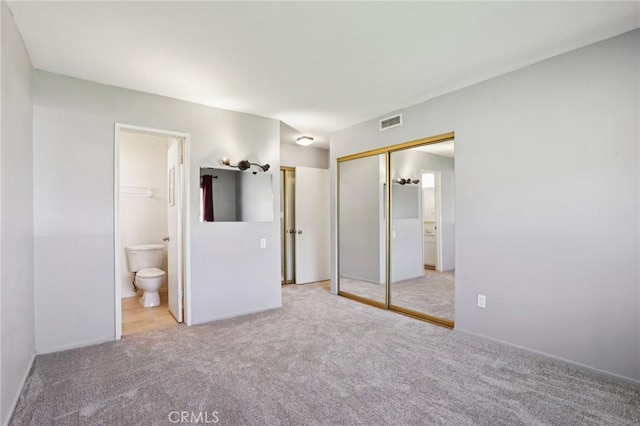 unfurnished bedroom featuring a closet, visible vents, light carpet, and ensuite bath