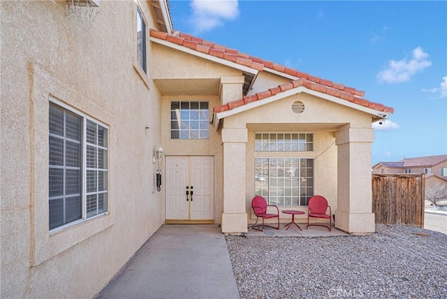 entrance to property featuring a tile roof, a patio area, fence, and stucco siding