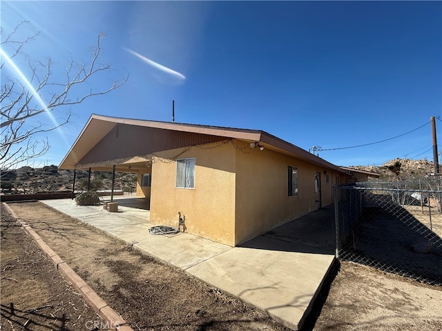 view of side of home with a patio area, fence, and stucco siding