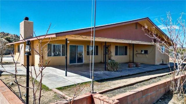 rear view of property featuring a chimney, a patio area, and stucco siding