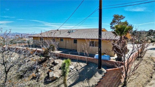 rear view of house featuring a patio area, roof with shingles, and stucco siding