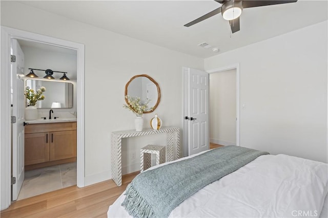 bedroom featuring visible vents, light wood-style floors, a ceiling fan, ensuite bath, and baseboards