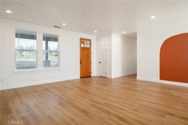 empty room with baseboards, visible vents, arched walkways, light wood-style floors, and recessed lighting