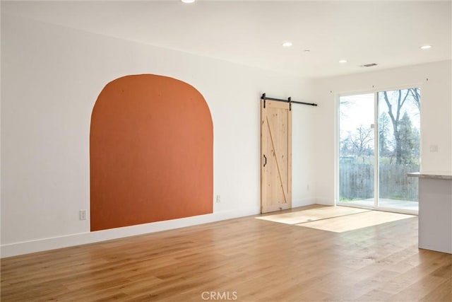 spare room featuring light wood-style floors, a barn door, baseboards, and recessed lighting