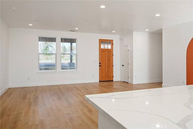 foyer entrance featuring baseboards, light wood-type flooring, arched walkways, and recessed lighting