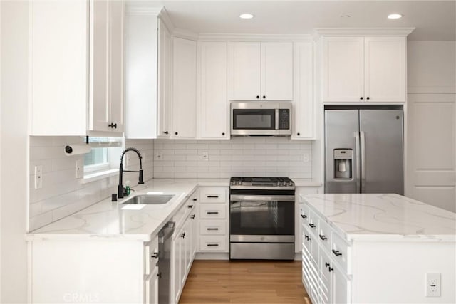 kitchen featuring stainless steel appliances, a sink, light stone countertops, and white cabinets