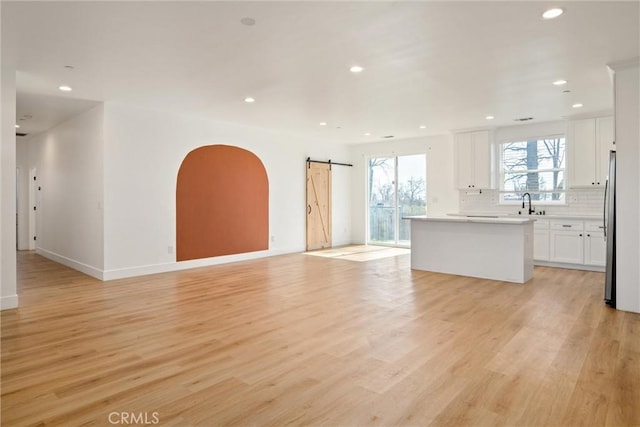 unfurnished living room with light wood-type flooring, a sink, recessed lighting, and a barn door