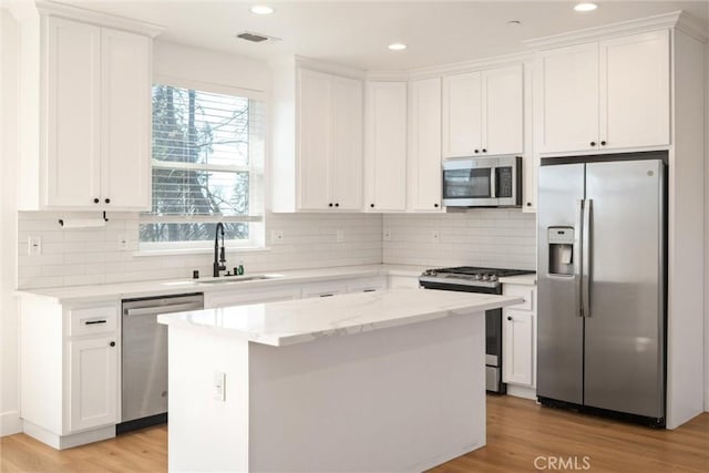 kitchen featuring a center island, light wood-style flooring, appliances with stainless steel finishes, white cabinetry, and a sink