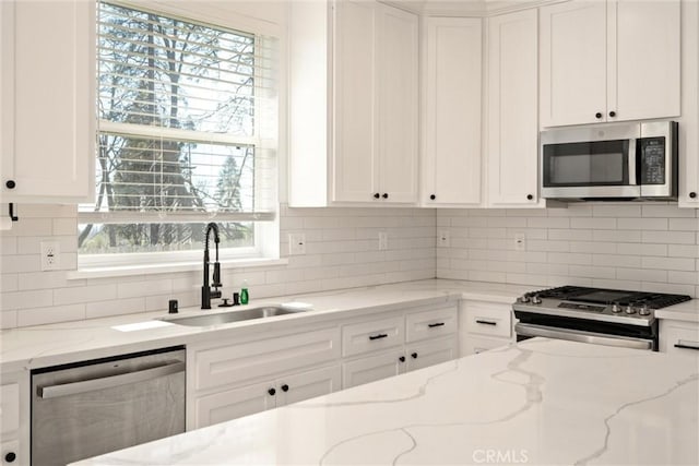 kitchen with white cabinetry, light stone counters, stainless steel appliances, and a sink