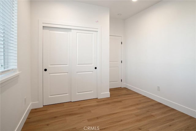 unfurnished bedroom with a closet, baseboards, and light wood finished floors