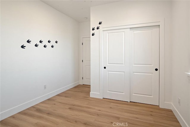 unfurnished bedroom featuring light wood-style flooring, baseboards, and a closet