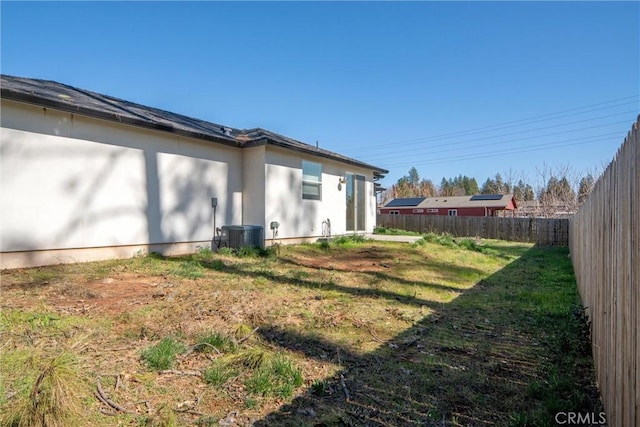 rear view of property featuring central air condition unit, stucco siding, a fenced backyard, and a yard