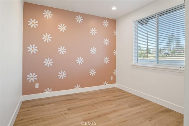 empty room with an accent wall, wallpapered walls, baseboards, and wood finished floors