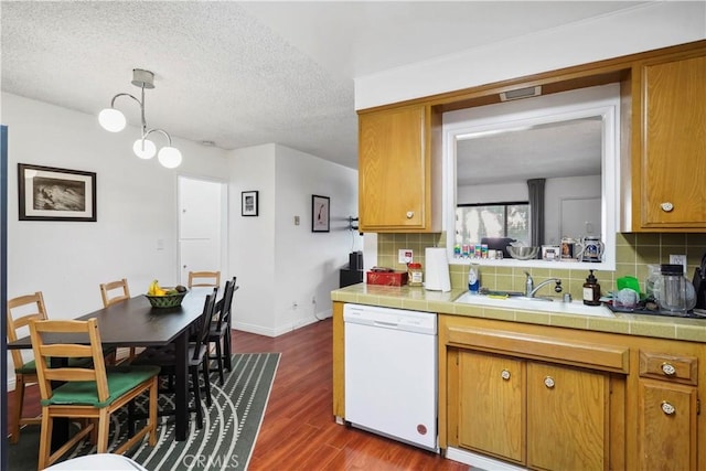 kitchen with tile counters, brown cabinets, white dishwasher, and a sink