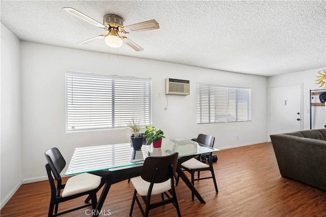 dining area with ceiling fan, a textured ceiling, an AC wall unit, and wood finished floors