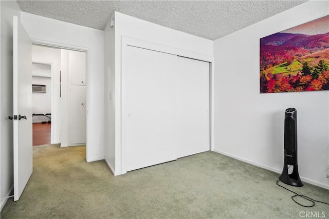 unfurnished bedroom with a wall unit AC, a closet, light colored carpet, a textured ceiling, and baseboards