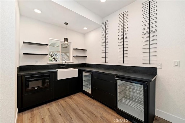 bar with light wood finished floors, wine cooler, black microwave, and a sink