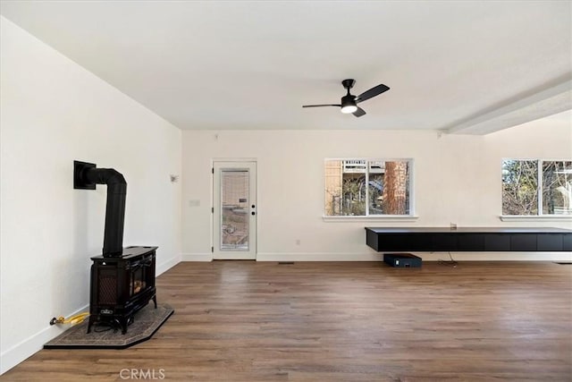 unfurnished living room featuring baseboards, wood finished floors, a wood stove, and a ceiling fan