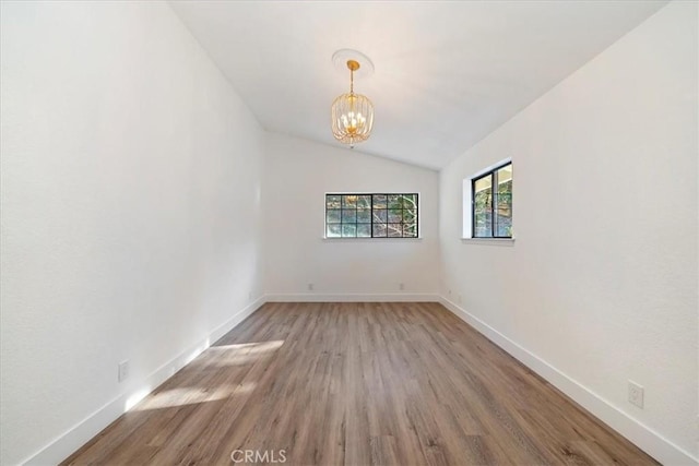 unfurnished room featuring light wood-type flooring, an inviting chandelier, baseboards, and vaulted ceiling