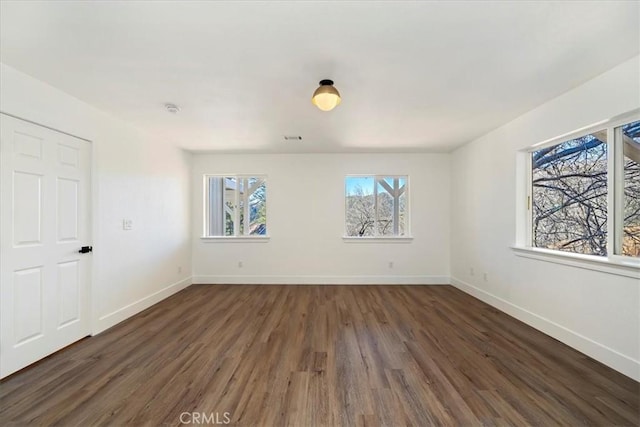 unfurnished room featuring visible vents, dark wood finished floors, and baseboards