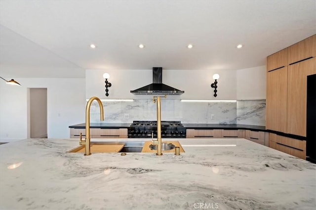 kitchen with tasteful backsplash, range, wall chimney exhaust hood, modern cabinets, and light stone counters