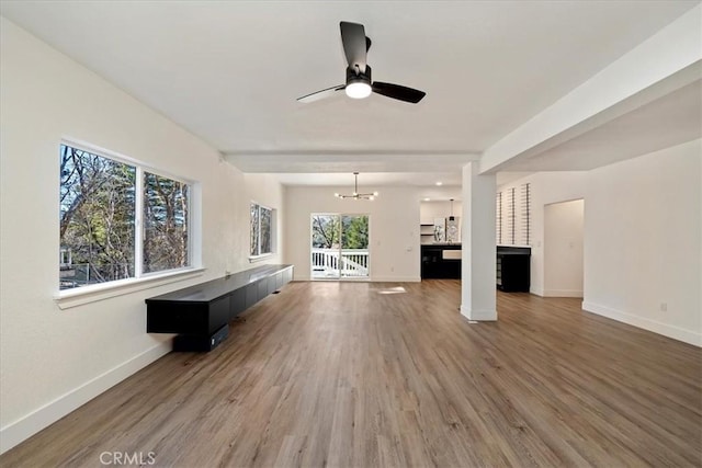 unfurnished living room with ceiling fan with notable chandelier, light wood finished floors, and baseboards