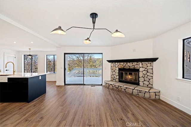 unfurnished living room with a wealth of natural light, a sink, a stone fireplace, and wood finished floors