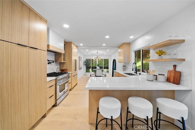 kitchen with modern cabinets, high end stainless steel range, a peninsula, light countertops, and a sink