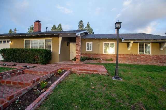 ranch-style home featuring brick siding, a chimney, stucco siding, a garage, and a front lawn