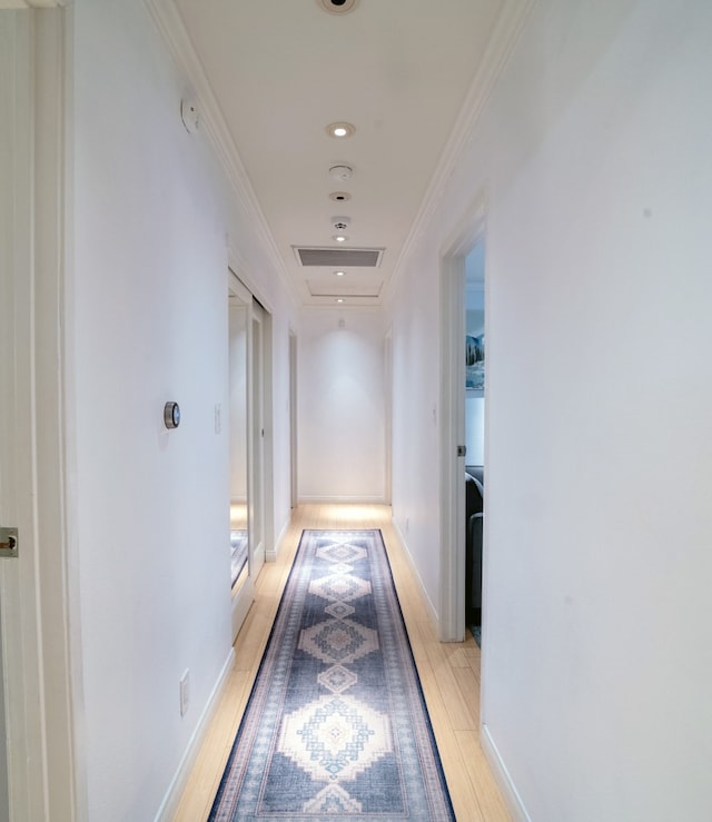 corridor featuring crown molding, light wood-style flooring, and baseboards