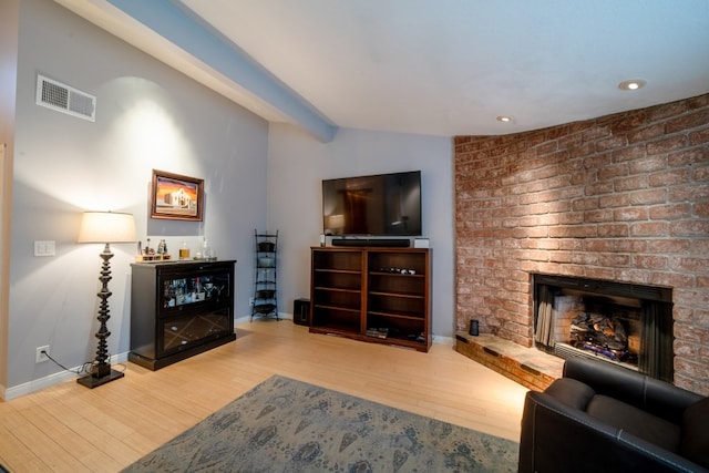 living area featuring lofted ceiling with beams, wood finished floors, visible vents, baseboards, and a brick fireplace