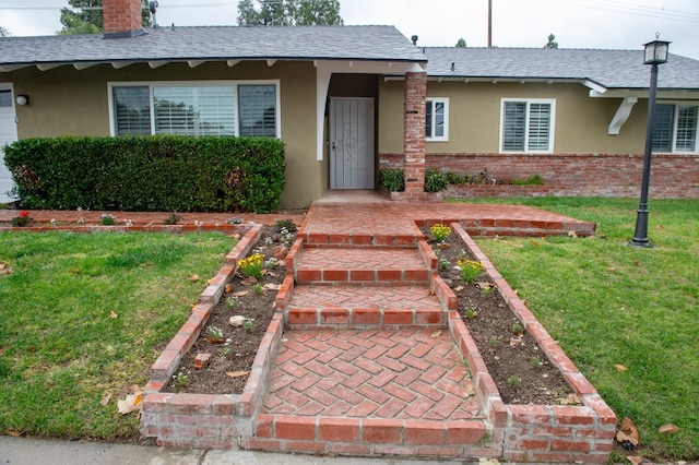 ranch-style house with a shingled roof, stucco siding, a chimney, a front lawn, and brick siding