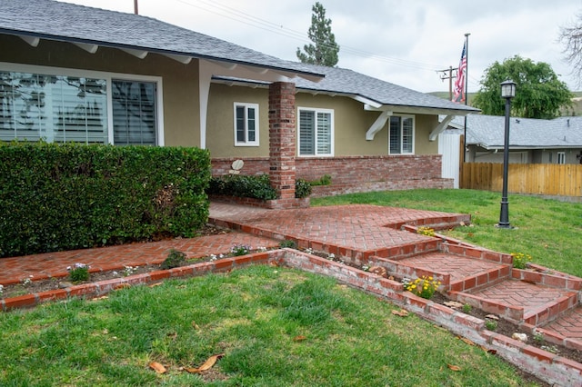 view of side of home featuring brick siding, a yard, stucco siding, a shingled roof, and fence