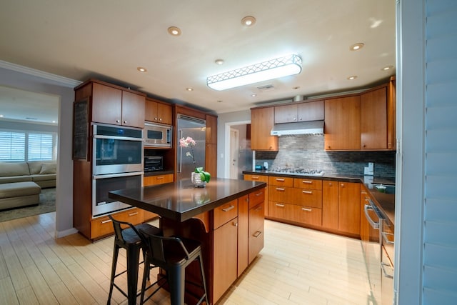 kitchen featuring tasteful backsplash, dark countertops, under cabinet range hood, and built in appliances