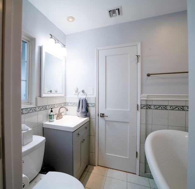 full bath featuring visible vents, toilet, tile patterned flooring, a freestanding bath, and tile walls