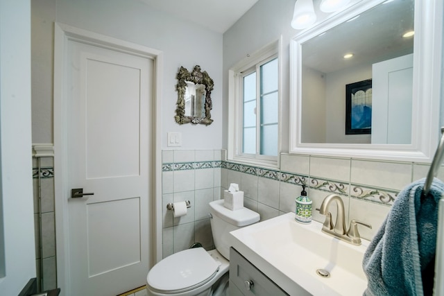 half bath with toilet, tile walls, and vanity