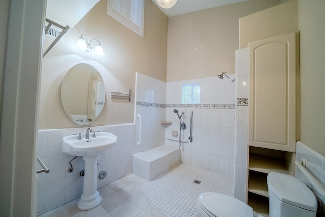 bathroom with a tile shower, tile walls, toilet, and tile patterned floors