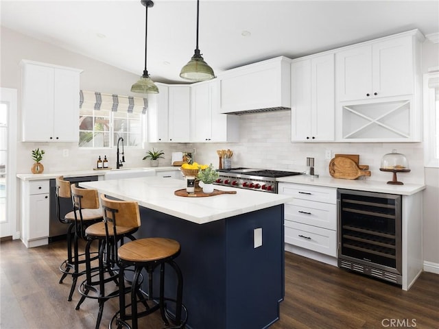 kitchen with decorative light fixtures, light countertops, white cabinetry, a kitchen island, and beverage cooler