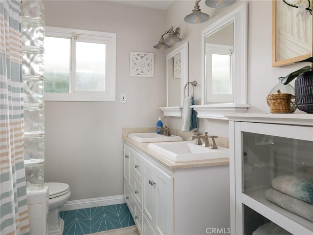 bathroom featuring toilet, double vanity, baseboards, and a sink