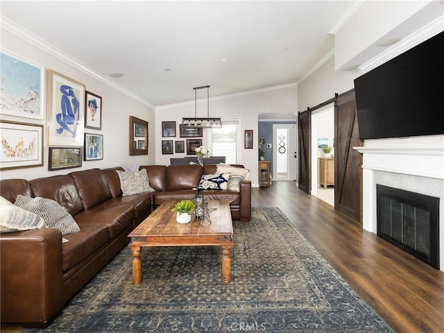 living area with ornamental molding, a glass covered fireplace, dark wood finished floors, and a barn door