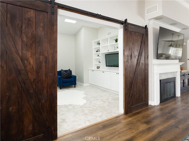 interior space with a barn door, baseboards, visible vents, a glass covered fireplace, and wood finished floors