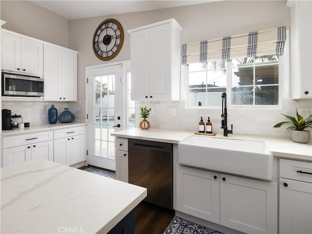 kitchen with black dishwasher, stainless steel microwave, backsplash, white cabinetry, and a sink