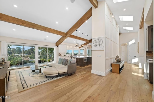 living room featuring a skylight, high vaulted ceiling, light wood-style floors, and beam ceiling