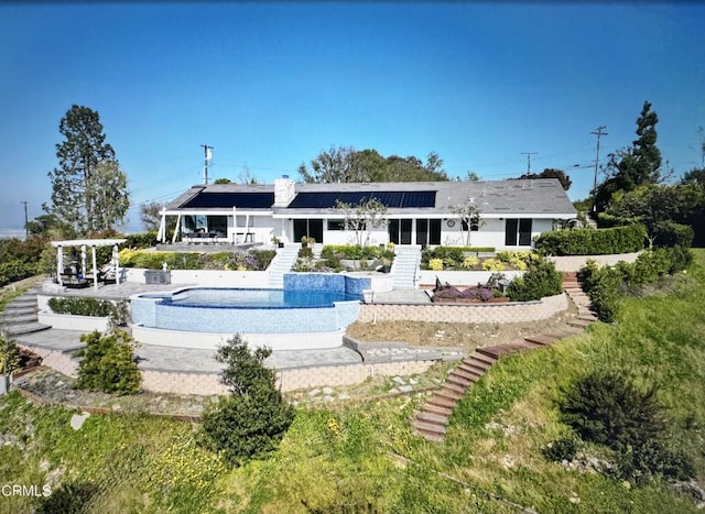 back of house with a patio area, a pergola, an outdoor pool, and solar panels